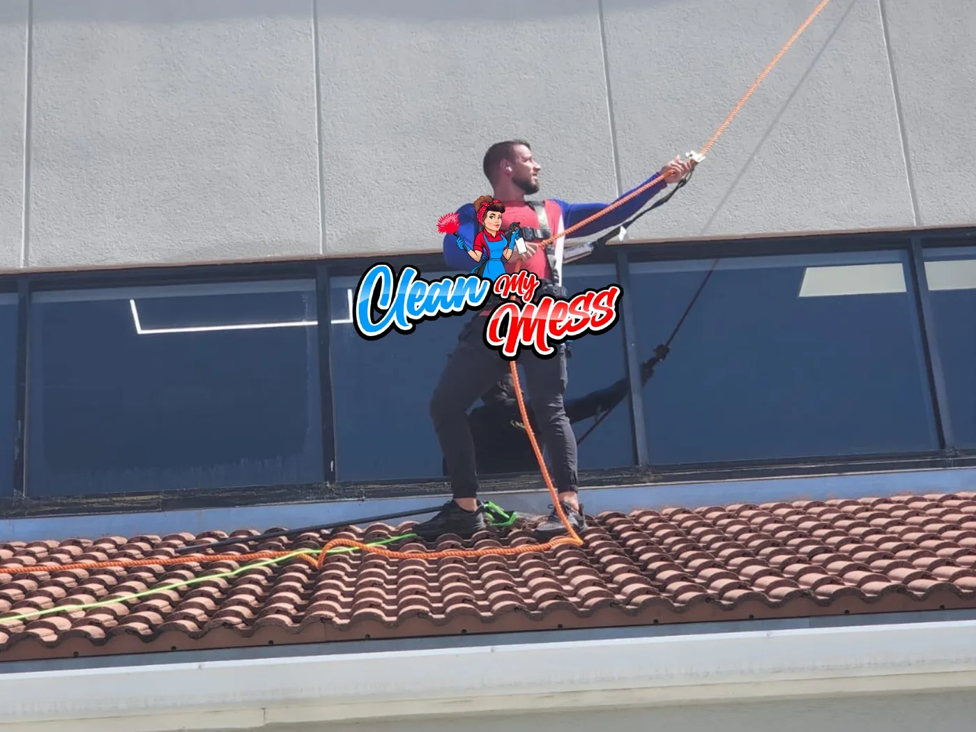 Clean My Mess cleaner on a roof washing a tall glass facade with a water-fed pole